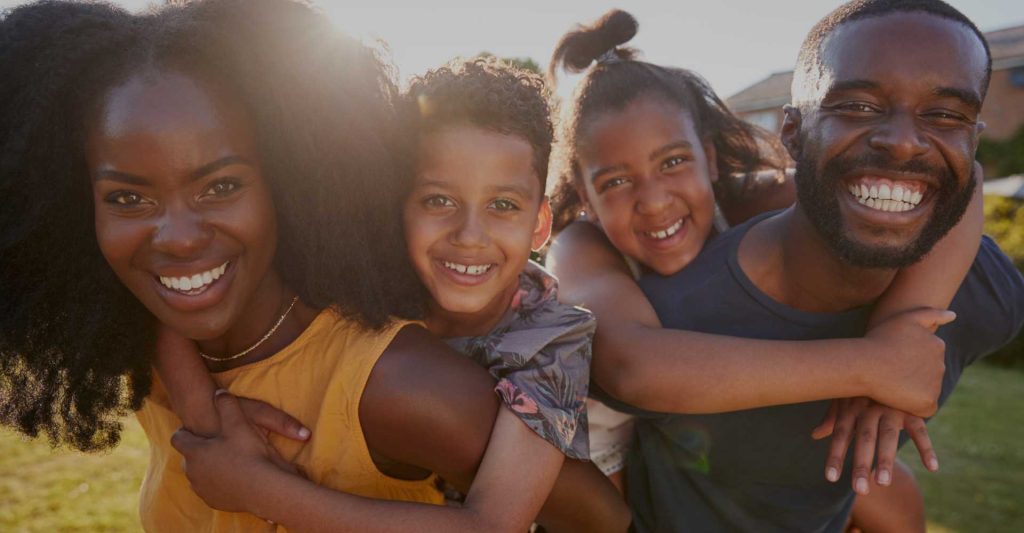 Black parents smiling with their son and daughter outdoors.