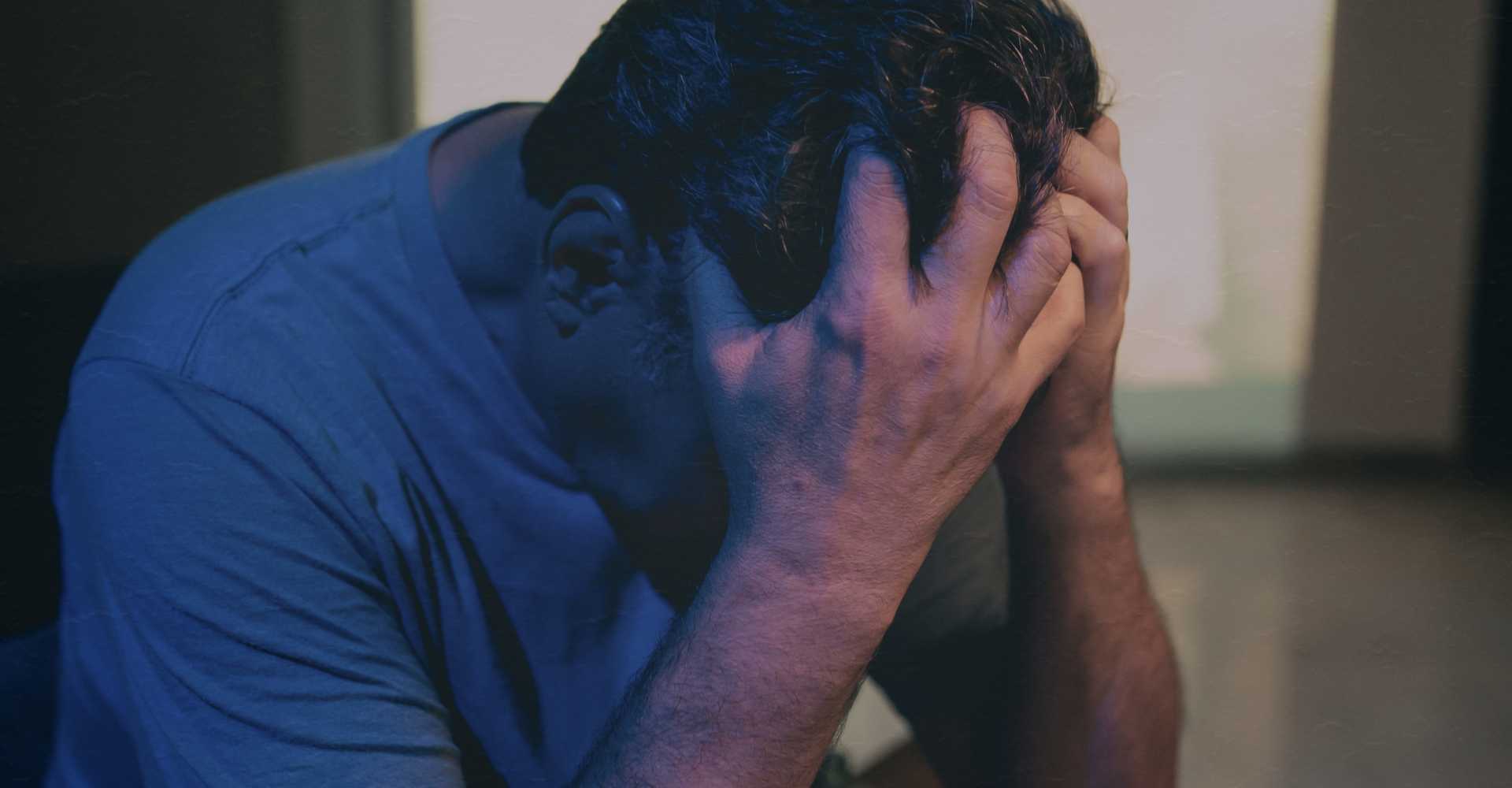 White man sitting on the ground with his face buried in his hands