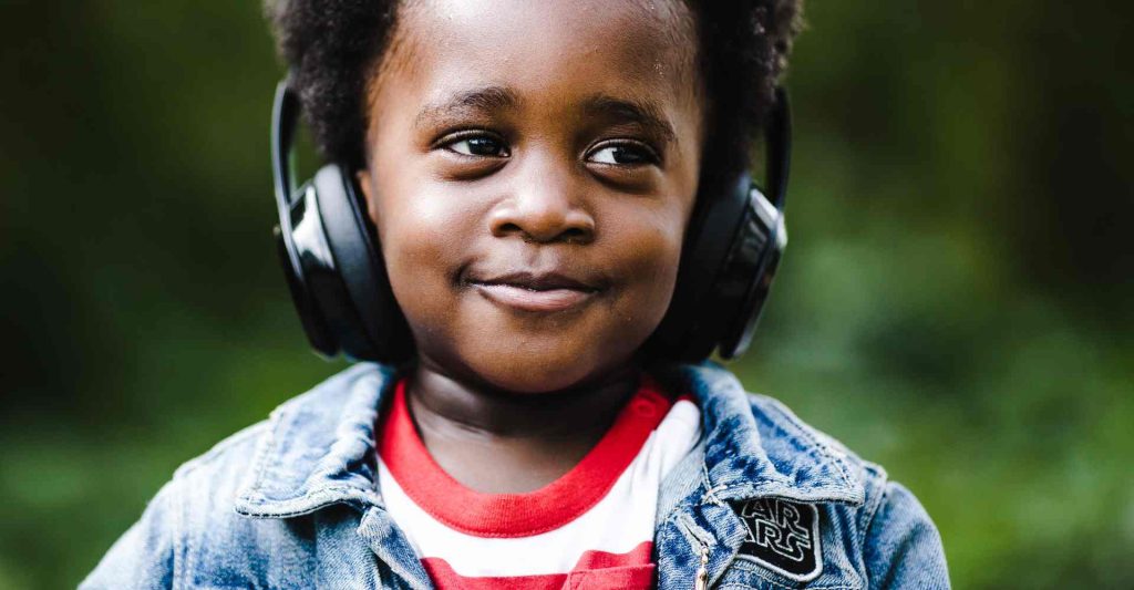 Young Black boy wearing headphones outside with a smile on his face.