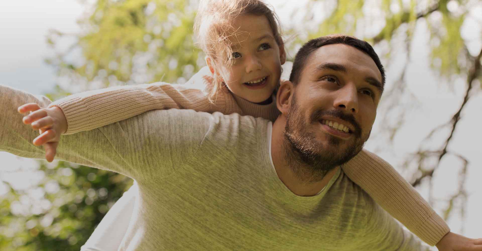 White dad with his young daughter on his back, both doing the superhero pose with their arms.