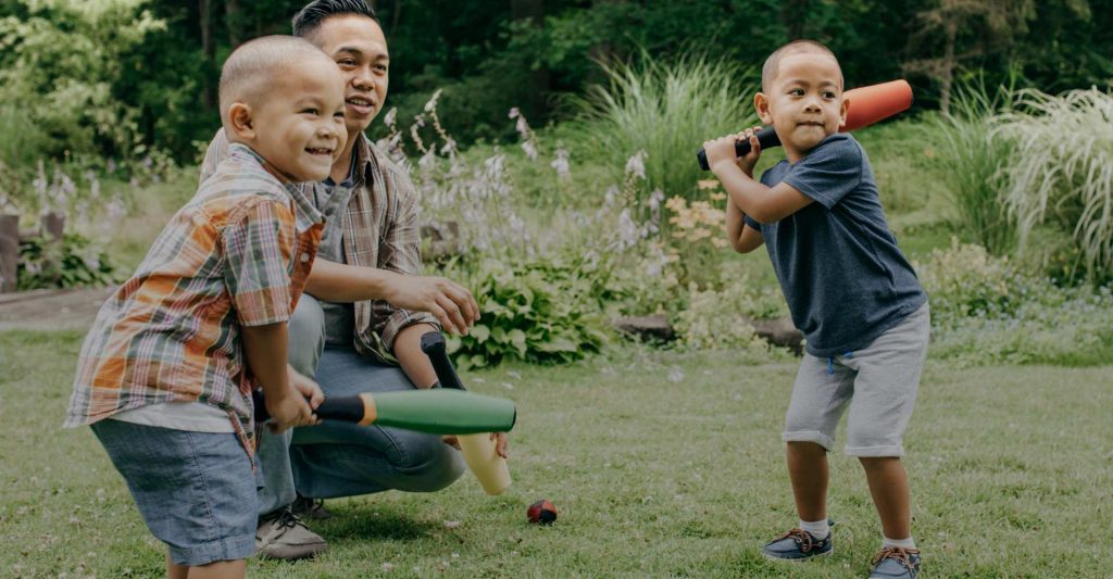 Asian dad teaching baseball joyfully to both of his sons holding bats