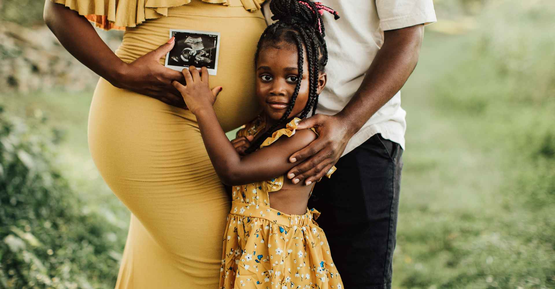 Black mom and dad holding daughter while daughter hugs mom holding ultrasound.