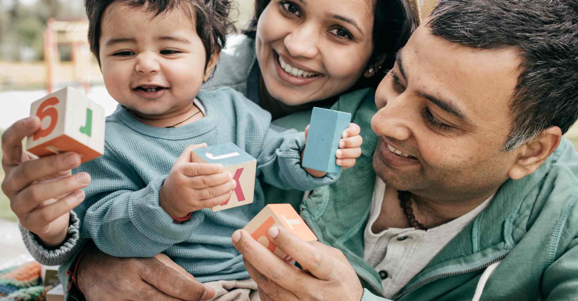 Arab mom and dad playing with blocks, laughing with their young son.