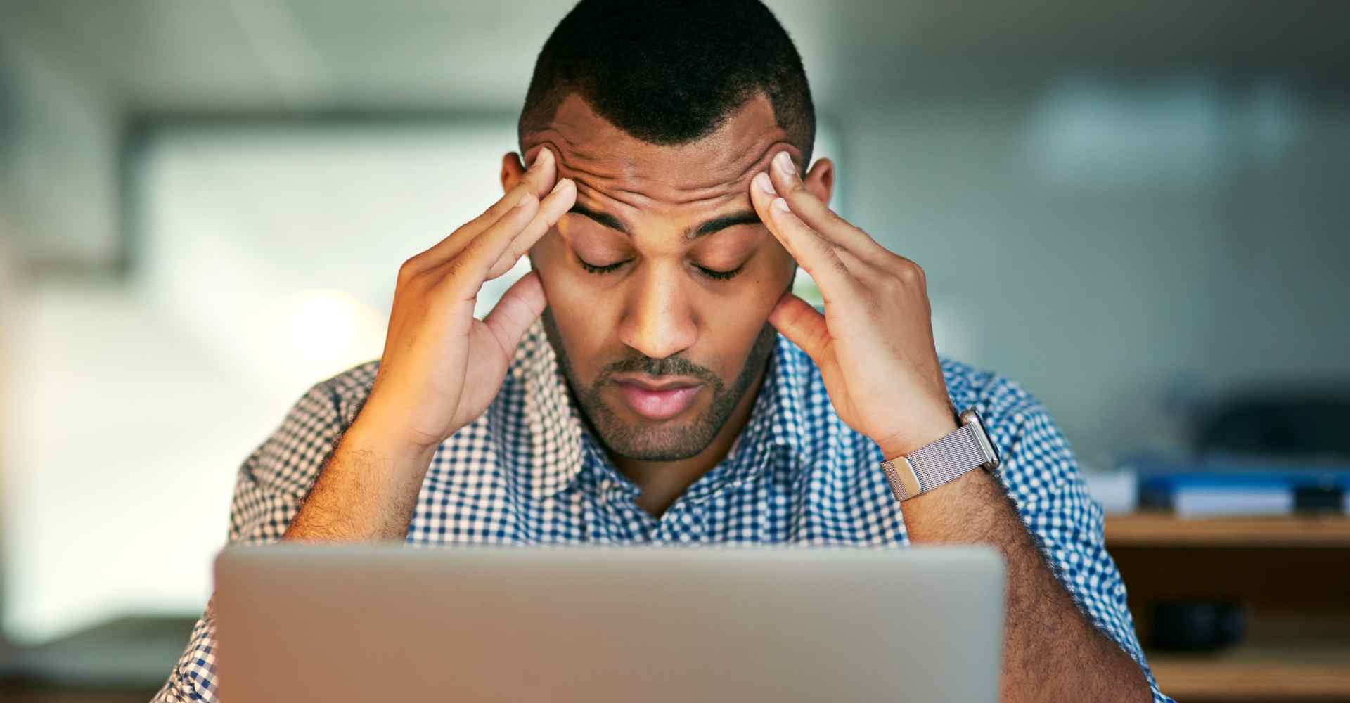 Man working on computer rubbing his forehead and closing his eyes in distress.