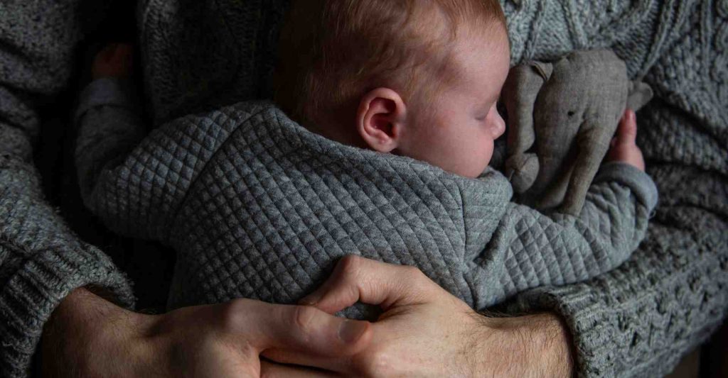 Dad cuddling his newborn baby holding a stuffed animal.