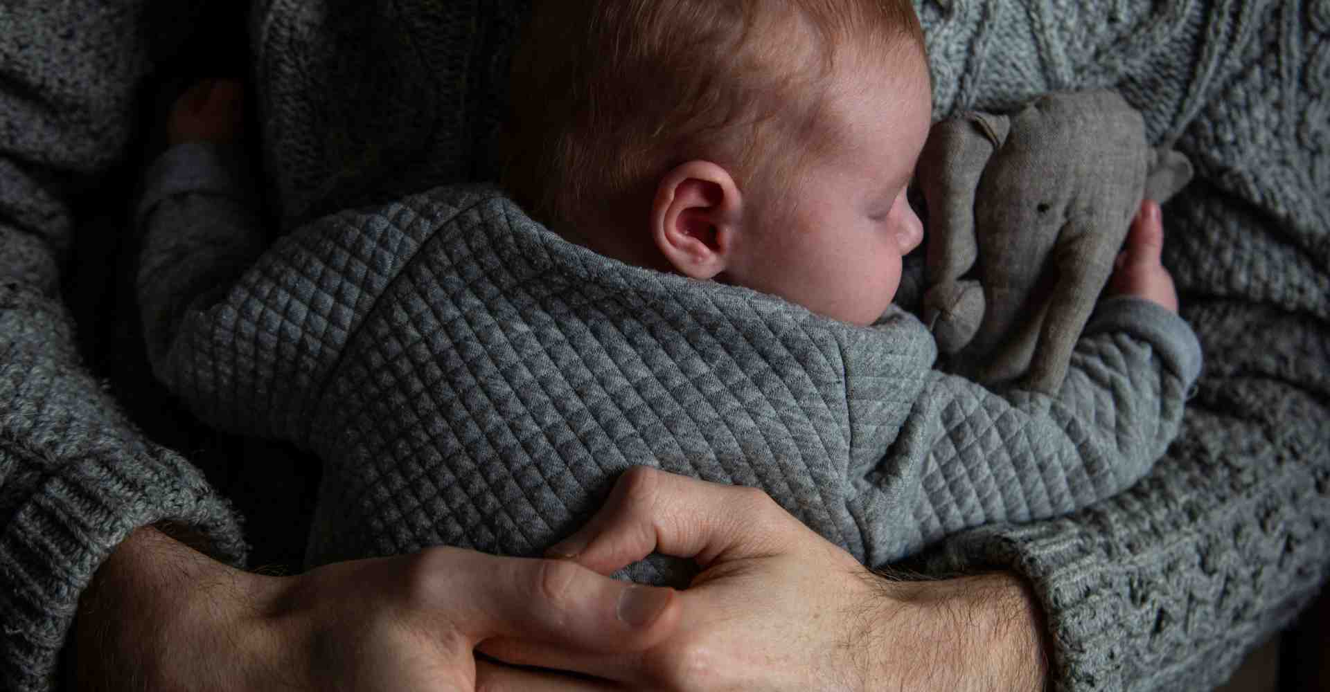 Dad cuddling his newborn baby holding a stuffed animal.