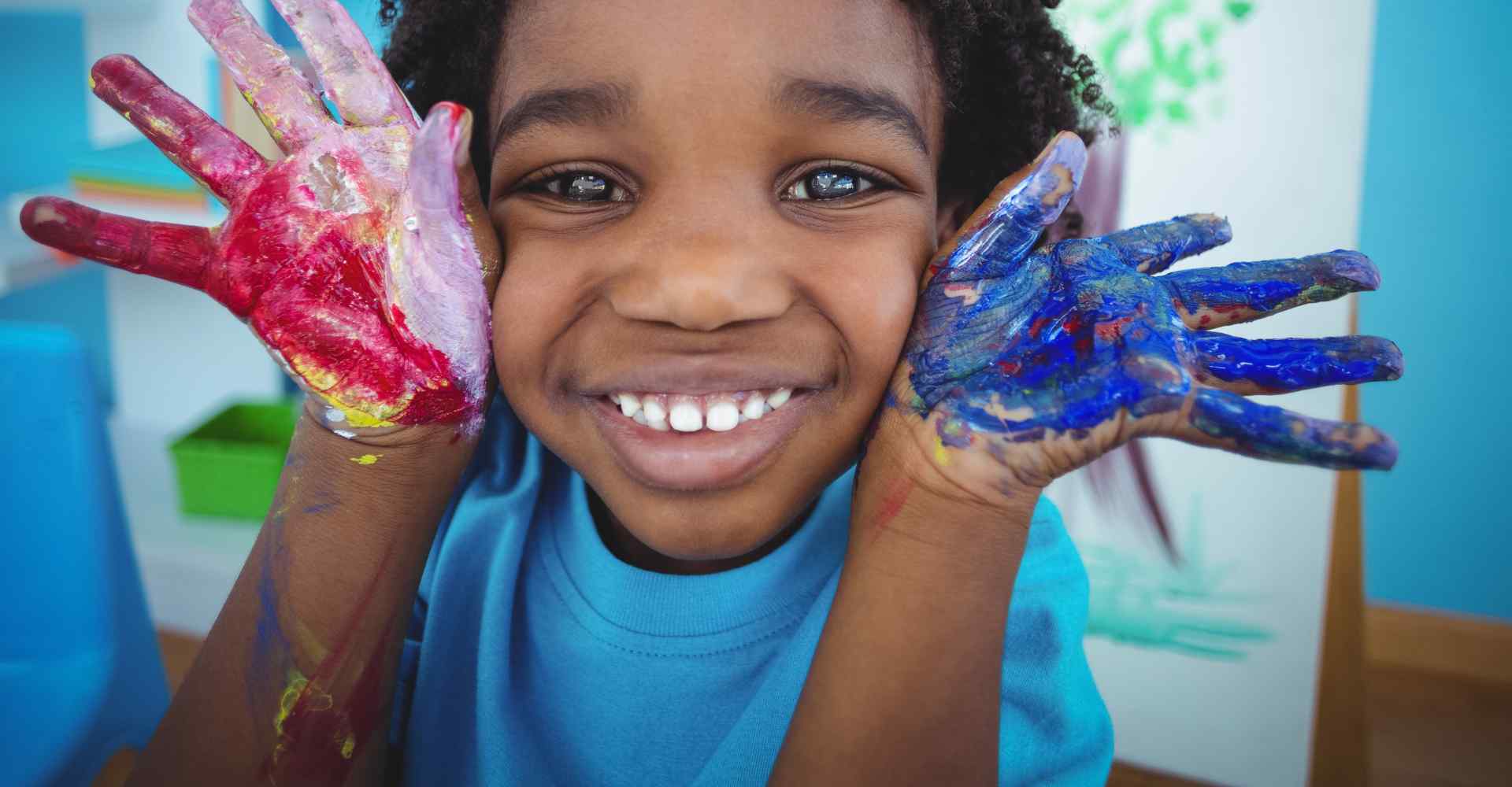 Joyful Black boy doing arts and crafts with colorful paint on his hands and arms.