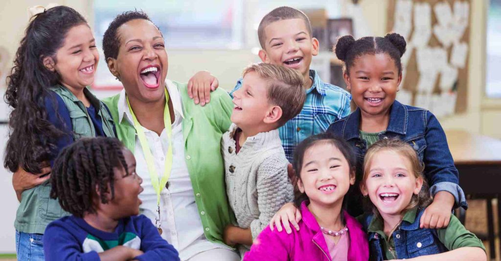 Black teacher laughing while interacting with diverse group of students joyfully