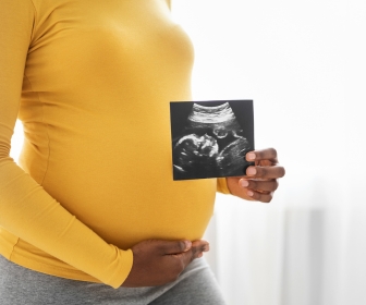 Black pregnant mom holding an ultrasound of her baby.