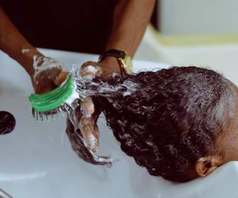 Black woman's hair being brushed and product being put in at salon. 