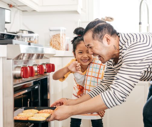 Asian dad and daughter joyfully getting cookies out of oven.