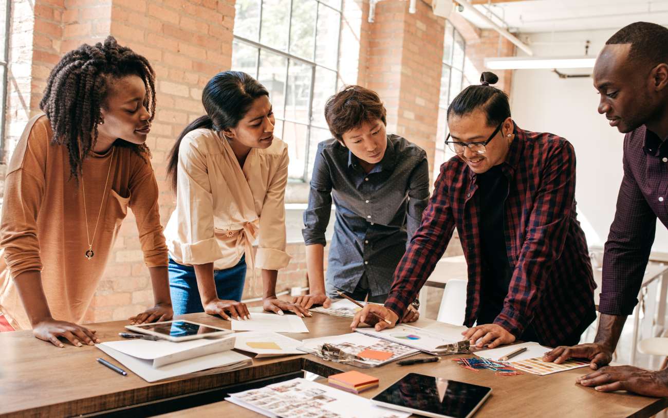 Diverse group of innovators discussing a project standing at a table.