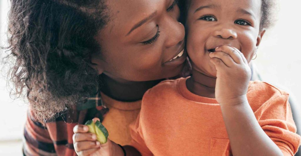 Black mom holding her child and laughing into her cheek.