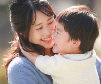 Asian mom and son hugging and playing with each other with big smiles on their faces.