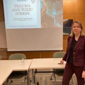 Clinical Institute fellow Reinhild Boehme posing next to her PowerPoint slides on Trauma and Toxic Stress. Our 2023 Institute Updates are fueled by the hard work of staff like Reinhild!