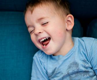 Young white boy laughing on the couch with joy.