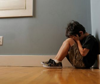 Young boy experiencing childhood toxic stress crying in the corner of a room. 