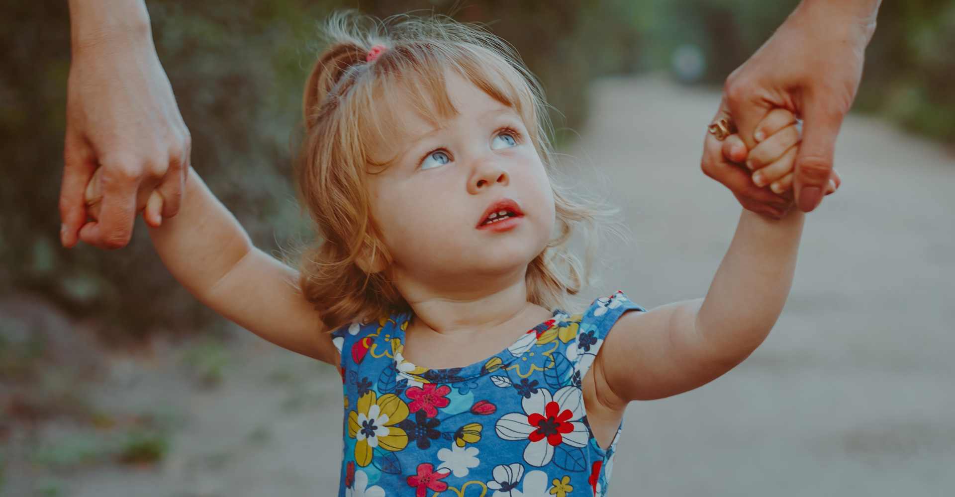 Little girl with curious expression holding both of her parents hands, looking up.