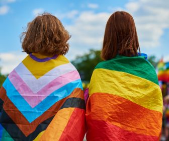 Back of two LGBTQ+ youth with LGBTQ+ flags