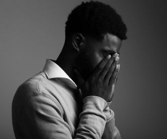 Black man experiencing shame with his face buried in his hands.