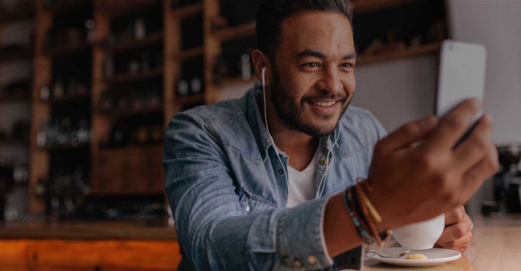 Hispanic man wearing headphones and smiling while listening to his counselor on a video call on his phone.