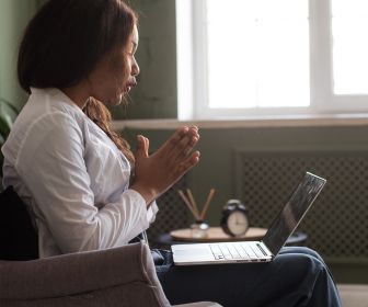 Biracial telehealth counselor using her hands to talk in a video call with a client.