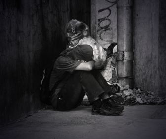 Unhoused person sitting in an alleyway next to trash in isolation from society due to mental health stigma.