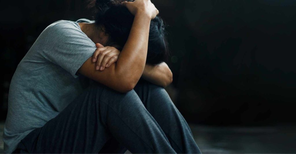 Distressed woman with her head on her knees sitting on the floor with hands wrapped around knees and head.