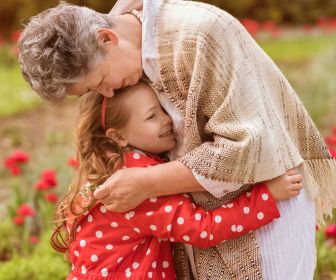 White grandma and granddaughter hugging in a field of flowers. Intergenerational healthy family dynamics being shown.