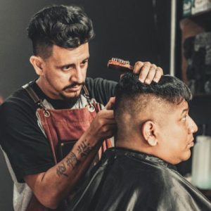 Hispanic hair stylist cutting a Hispanic man's hair.