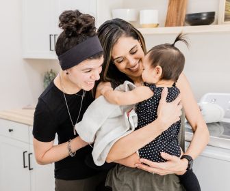 Hispanic and white lesbian couple holding their daughter. 