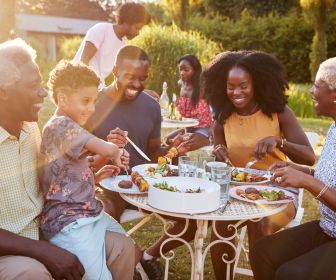 Black intergenerational family sitting outside joyfully eating together.