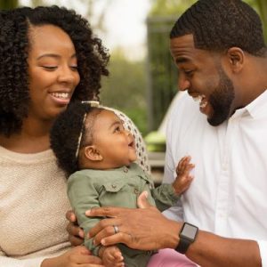 Black mom and dad holding their baby daughter smiling joyfully during a photoshoot.