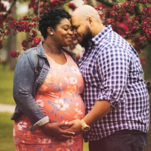 Black pregnant woman embracing husband during a maternity photo shoot.